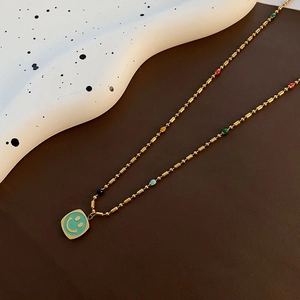 Collana in acciaio al titanio dorato con ciondolo smiley in smalto blu e perle colorate