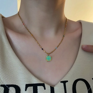 Collana a sfere dorate con ciondolo quadrato smiley blu indossata da una modella