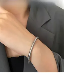 Detail of silver spiral snake-style steel bracelet on model wrist with grey blazer