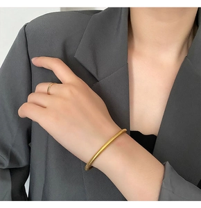 Detail of a gold spiral texture bracelet and minimalist ring worn with a grey blazer