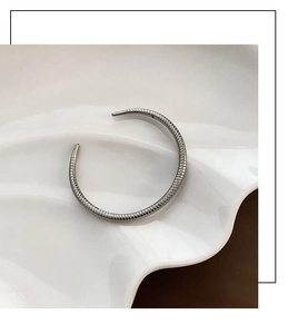 Detail of silver asymmetric cuff bracelet featuring textured segments on a white tray