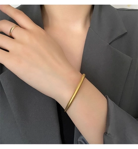 Detail of gold snake-patterned spiral bangle with minimalist ring on elegant grey blazer