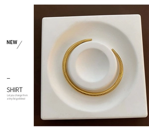 Detail view of a gold-toned rigid snake texture choker on a white display tray