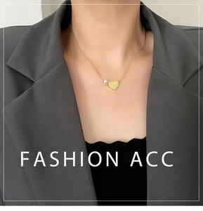 Detail of gold heart pendant and pearl on snake chain necklace worn by a model