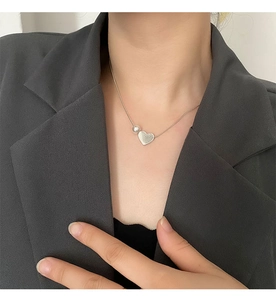 Detail of silver heart pendant with pearl on snake chain worn on a black blazer