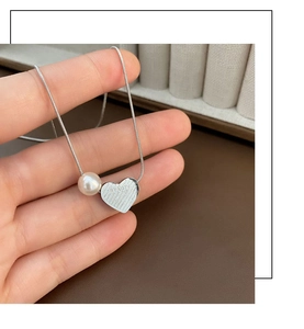 Detail of silver heart pendant with pearl and Beauty engraving on snake chain