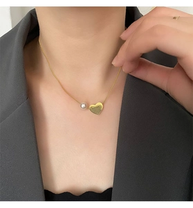 Detail of gold heart pendant with Beauty engraving and white pearl on model neck
