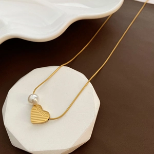 Golden titanium steel heart necklace with pearl and BEAUTY engraving on a stone pedestal