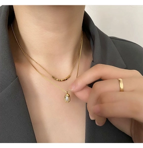 Détail d'un collier double rang doré avec perles carrées et pendentif en nacre sur mannequin
