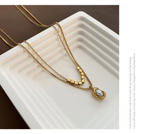 Détail d'un collier doré à deux rangs avec pendentif perle grise sur des marches blanches