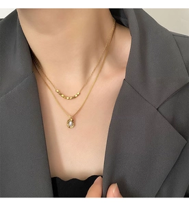 Détail d'un collier doré à deux rangs avec pendentif perle sur une tenue élégante