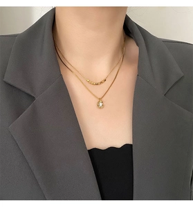 Gros plan d'un collier doré double couche avec billes d'or et pendentif perle irrégulier