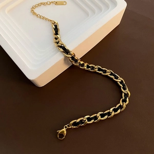 Luxurious gold chain bracelet woven with black cord featuring a lobster clasp and charm