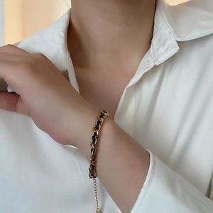 Luxurious gold titanium steel chain bracelet with woven black cord on a white shirt