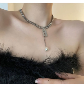 Detail einer silbernen Gliederkette mit B-Anhänger und Barockperle am Hals des Modells