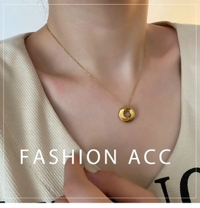 Detail of twisted gold donut pendant and delicate O-chain on female model neckline