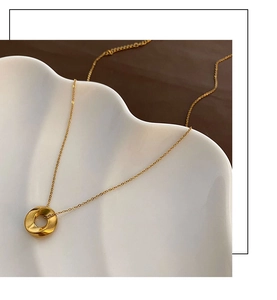 Macro view of golden twisted ring pendant on a fine O-chain over white ceramic tray