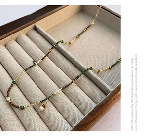 Macro detail of Bohemian beaded necklace with green beads and pearls on beige velvet