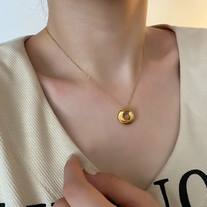 Golden twisted ring pendant on a fine O-chain necklace worn on a woman's collarbone