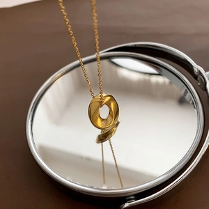 Minimalist twisted pendant gold necklace with o-chain design on a reflective mirror surface