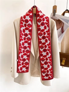 Détail d'un foulard en soie à fleurs de coquelicot rouge sur un blazer beige et sac
