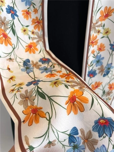Gros plan du foulard en soie montrant un imprimé marguerites orange et une texture satinée
