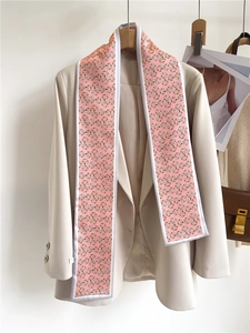 Detail of pink silk scarf with gold horsebit pattern styled on a beige blazer collar
