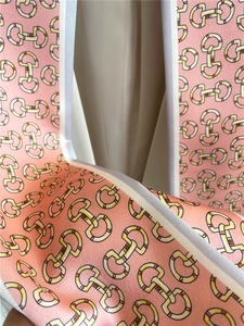 Detail of pink silk scarf featuring golden horsebit patterns and white contrast borders