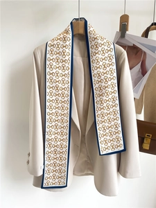 Close-up of elegant white silk scarf with gold horsebit print styled on a beige blazer