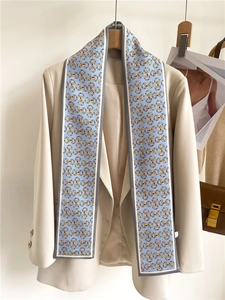 Detail of light blue silk scarf with golden horsebit print on a beige blazer