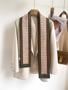 Detail of a thin silk scarf with horse-bit print styled on a cream-colored blazer
