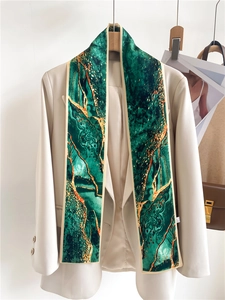 Détail d'un foulard en soie à motif marbre vert sur un blazer beige avec des accents dorés