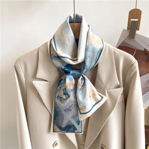 Détail d'un foulard en soie à motif marbré bleu et doré noué sur un revers de blazer
