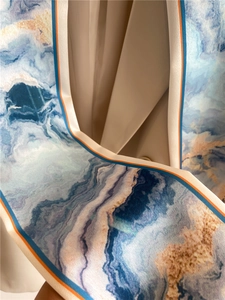 Détail d'un foulard en soie au motif marbré bleu avec une bordure orange contrastée