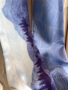 Gros plan d'une écharpe en soie à motif paysage bleu et vagues sur un costume beige