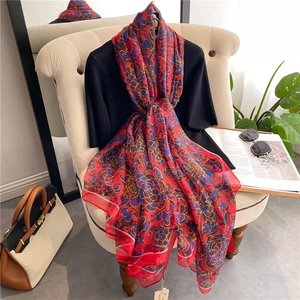Elegant red silk floral scarf with blue flowers draped on black knit top and beige chair