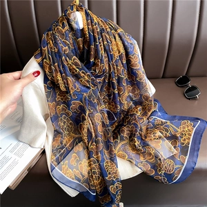 Navy blue silk scarf with golden floral patterns draped over white knitwear