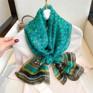 Close-up of green silk-feel scarf with colorful polka dots tied over a white sweater