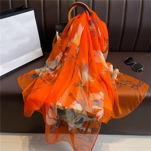 Detail of vibrant orange silk shawl with magnolia print draped on a stylish leather handbag