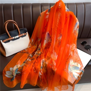 Detail of orange floral silk shawl draped on a sofa, featuring white magnolia flower print