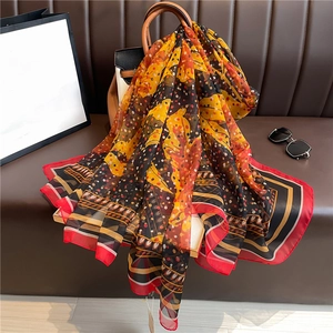 Close-up of tropical leaf and polka dot pattern on a silk-like scarf draped on a handbag