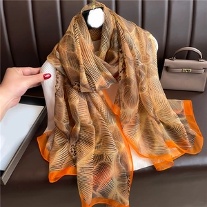 Detail of elegant brown leaf pattern scarf with vibrant orange hand-rolled edges