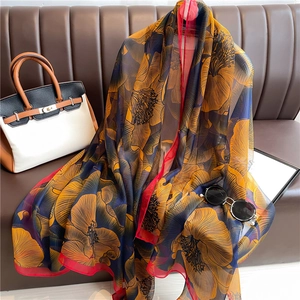 Detail of blue floral silk scarf with red rolled edges on a luxury leather bag background