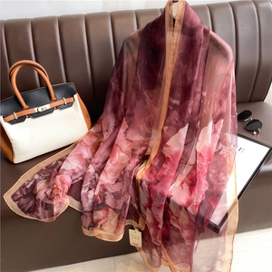 Elegant red and pink floral print silk shawl draped over a sofa with lifestyle accessories