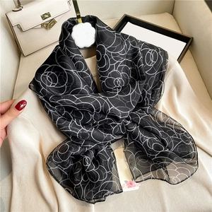 Elegant black silk scarf with white rose floral patterns over a beige sweater
