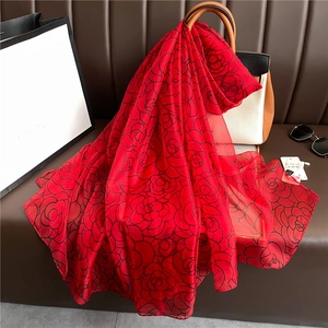 Elegant red silk shawl with black camellia floral patterns draped on a handbag