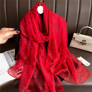 Detailed texture of red silk scarf with black rose patterns and hand showing soft material