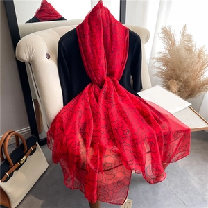 Detail of large red chiffon scarf with black rose pattern draped on black knit top