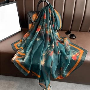 Elegant dark green floral silk scarf with orange borders draped on a leather handbag