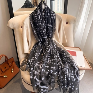 Detail of polka dot silk scarf draped over cream knitwear and orange luxury handbag